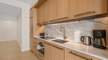 A modern kitchen with wooden cabinets, a marble countertop, a stainless steel sink, and a coffee machine.