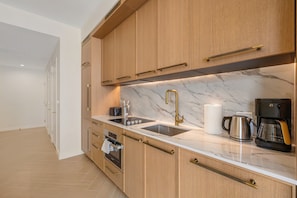 Une cuisine moderne avec des meubles en bois, un plan de travail en marbre, un évier en acier inoxydable et une machine à café.