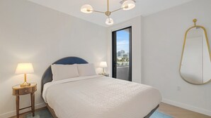 Un dormitorio con cama, lámparas de noche, una lámpara en el techo, vistas a través de una puerta y un espejo montado en la pared.