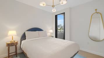 Quarto com cama, luminárias de cabeceira, luminária no teto, vista através de uma porta e um espelho fixado na parede.