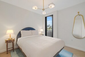 A bedroom with a bed, bedside lamps, a ceiling light fixture, a view through a door, and a wall-mounted mirror. - Miami Oasis 2BR Apartment with Pool (Miami)