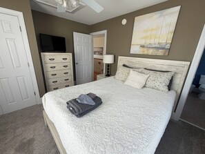 A bedroom with a bed, a dresser, a television, and a painting on the wall. - 4BR in Downtown Surf City • 1 Block to Beach (Surf City)