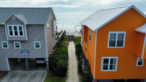 A coastal property with a wooden walkway leading to a beach, a garage, and a sign for a surf shop. - 4BR in Downtown Surf City • 1 Block to Beach (Surf City)
