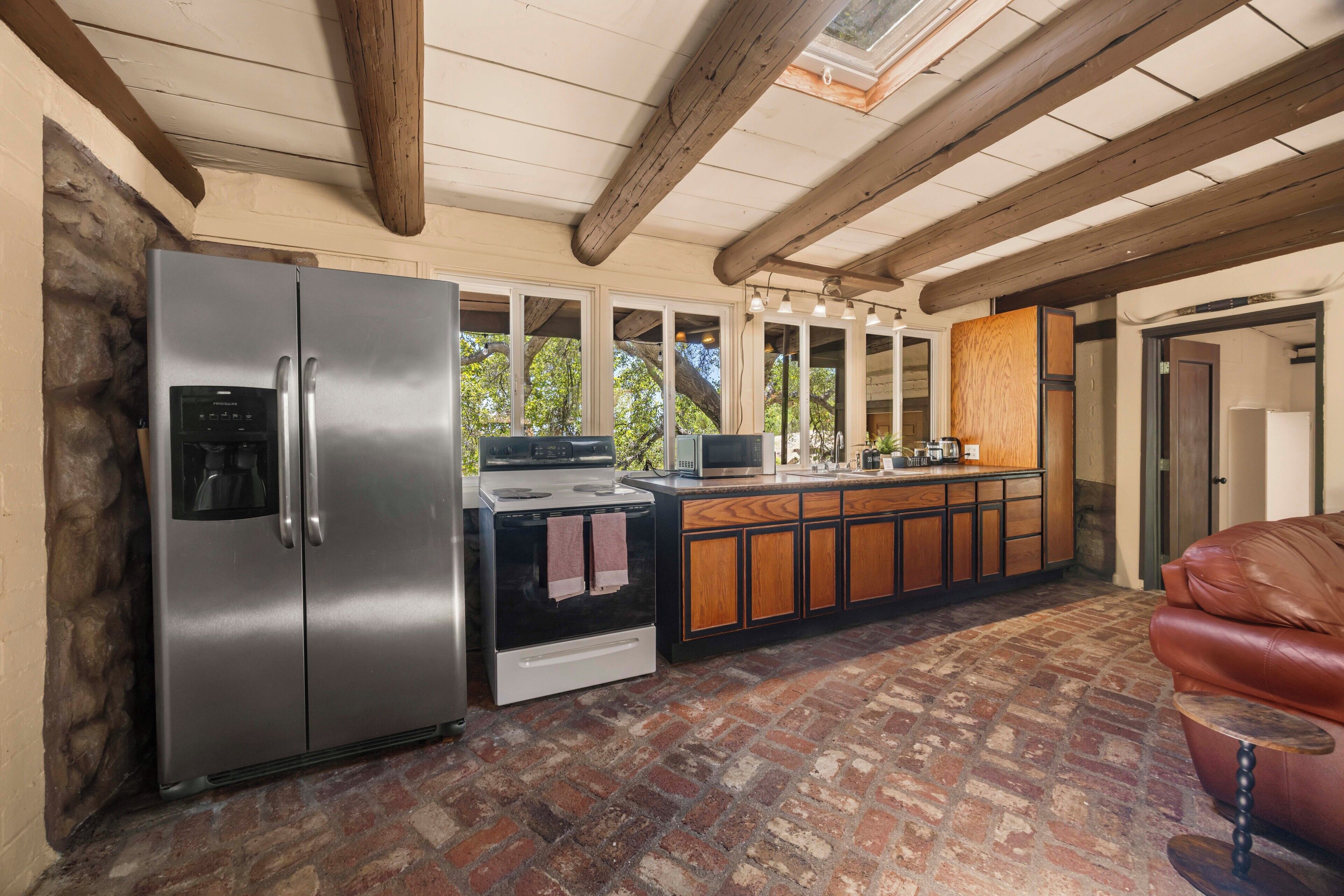A kitchen with a stainless steel refrigerator, a stove, and a microwave. There is a wooden cabinet and a coffee bar.