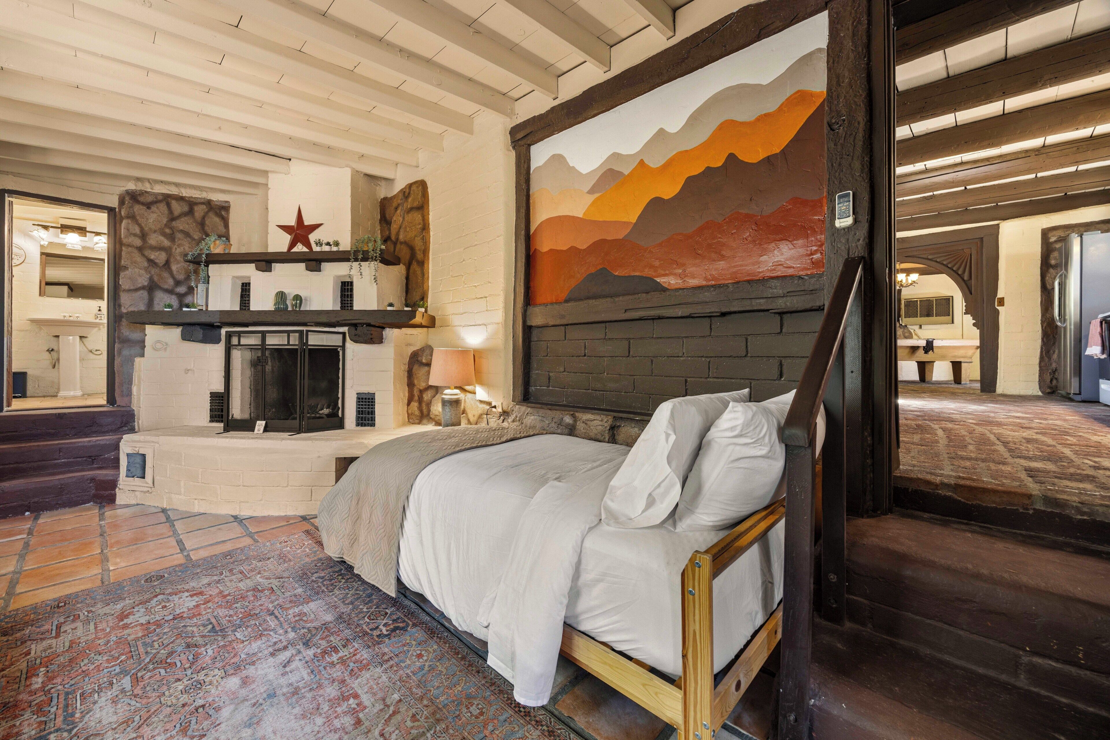 A bedroom with a bed, a fireplace, a stone wall, and a mural.