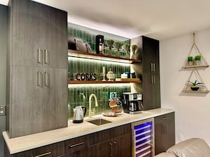 A modern kitchen with dark wood cabinets, a stainless steel coffee maker, and a built-in wine cooler. - Serenity Lake House . Private Lakefront Escape (Trail Creek)