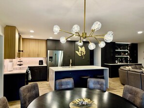 A modern kitchen with a central island, dark cabinetry, and a chandelier with multiple crystal lights. - Serenity Lake House . Private Lakefront Escape (Trail Creek)
