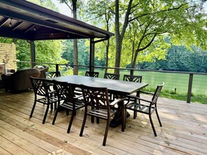 A covered outdoor deck with a table and chairs, overlooking a body of water and surrounded by trees. - Serenity Lake House . Private Lakefront Escape (Trail Creek)