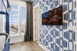 A hotel room with a large window, a bed, a wall-mounted TV displaying a cityscape, and a geometric patterned wall. - Rooftop deck townhome sleeps 12, minutes to Broadway, Nashville (Nashville)