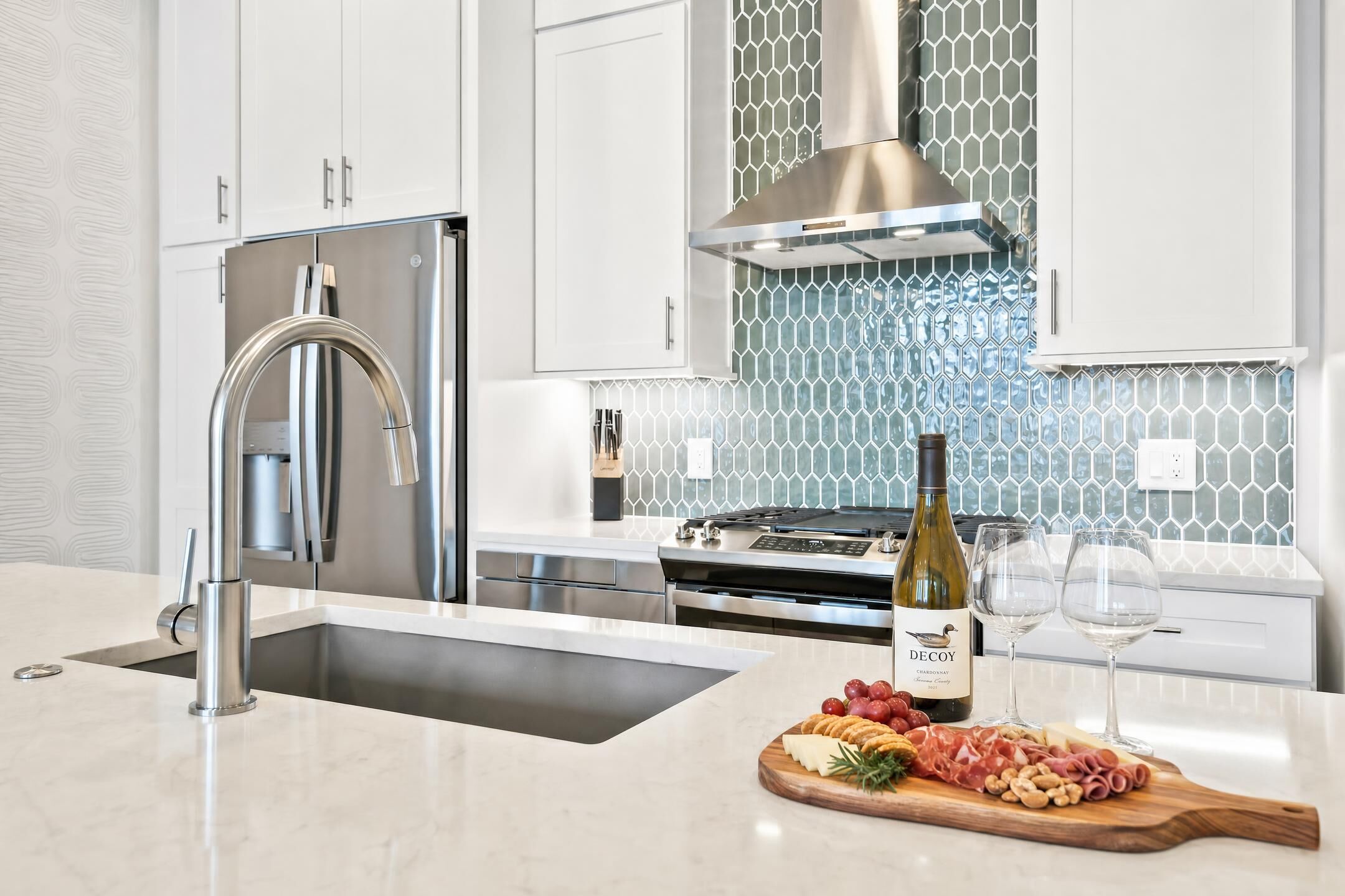 Una cocina moderna con electrodomésticos de acero inoxidable, horno empotrado y una botella de vino en la encimera.