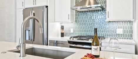 Una cocina moderna con electrodomésticos de acero inoxidable, horno empotrado y una botella de vino en la encimera.