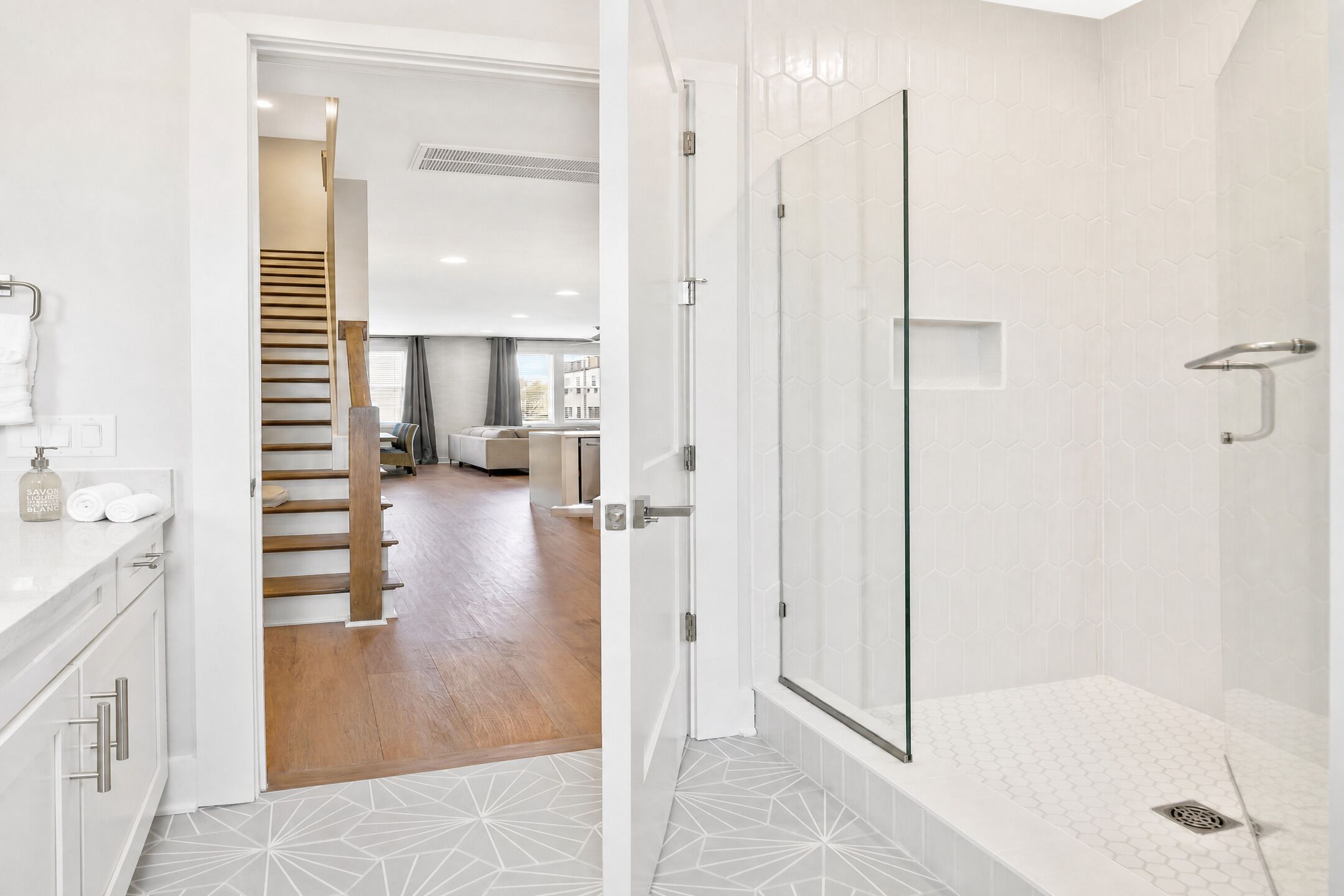 Une salle de bain moderne avec une douche à parois de verre, un carrelage blanc au sol et un distributeur de serviettes visible.