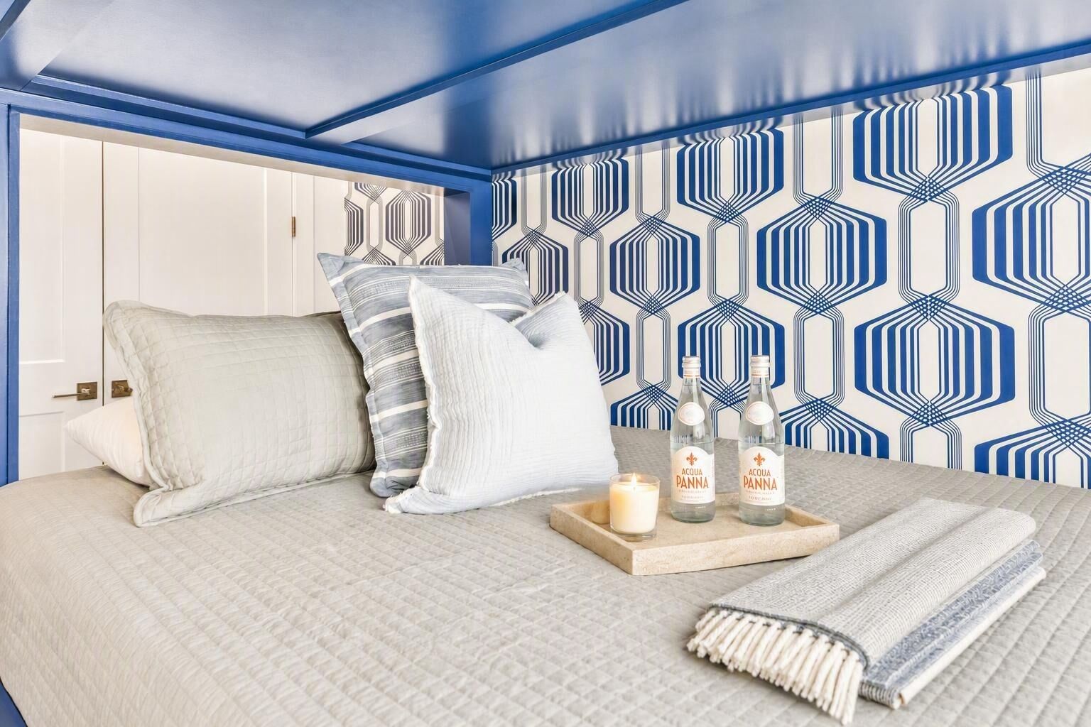 A bedroom with a bed, pillows, a tray with bottles, a candle, and a blanket.