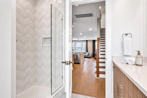 A modern bathroom with a glass shower enclosure, a wooden staircase, and a kitchen area visible through an open door. - 2 rooftop homes near Broadway & Geodis Park, sleeps 24 (Nashville)