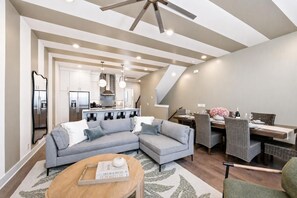 A modern living room with a grey sectional sofa, a dining area with wicker chairs, and a kitchen with stainless steel appliances. - 2 rooftop homes near Broadway & Geodis Park, sleeps 24 (Nashville)