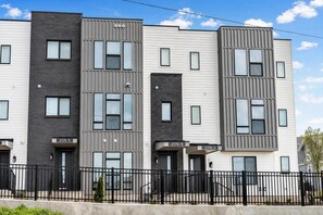 A multi-story residential building with a modern architectural design, featuring a mix of white and dark grey exterior panels, multiple windows per floor, and a black metal fence in the foreground. - 2 rooftop homes near Broadway & Geodis Park, sleeps 24 (Nashville)