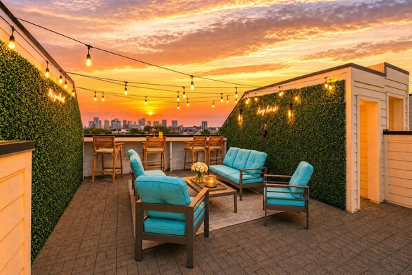 An outdoor seating area with chairs and a table, a city skyline in the background, and string lights. - 2 rooftop homes near Broadway & Geodis Park, sleeps 24 (Nashville)