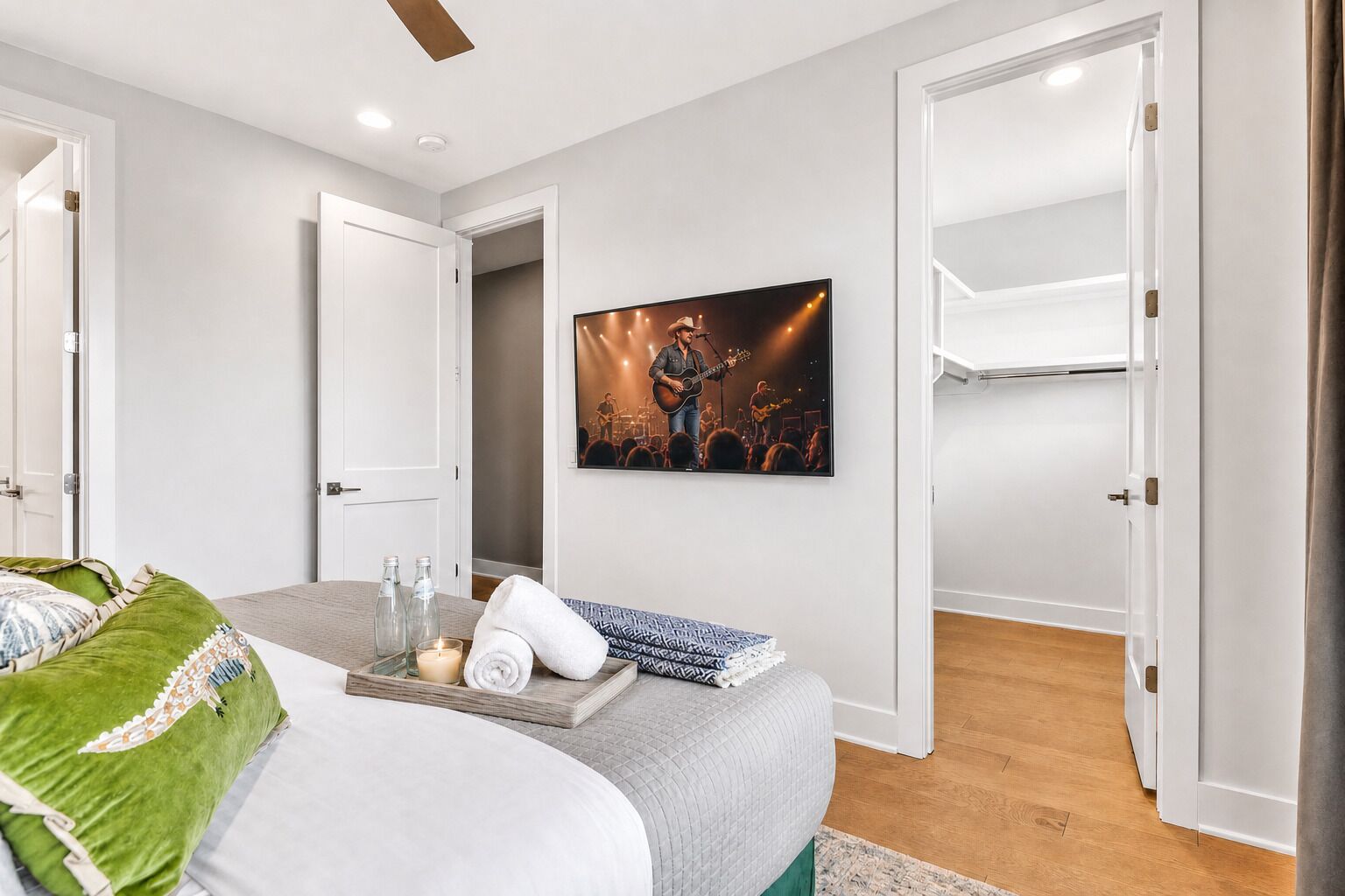 A bedroom with a bed, a bedside table with candles, a framed picture on the wall, and a door leading to another room.