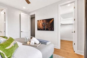 A bedroom with a bed, a bedside table with candles, a framed picture on the wall, and a door leading to another room. - 2 rooftop homes near Broadway & Geodis Park, sleeps 24 (Nashville)