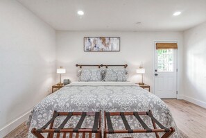 Un dormitorio con cama, dos mesitas de noche, una puerta y ventana con vistas.