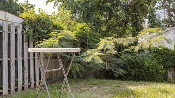 Une table ronde dotée d’un cadre en métal, placée dans une cour arrière verdoyante, avec une clôture en bois et un feuillage dense en arrière-plan.
