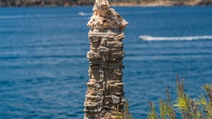 Paisatge costaner amb una roca destacada en primer pla i una massa d'aigua al fons.