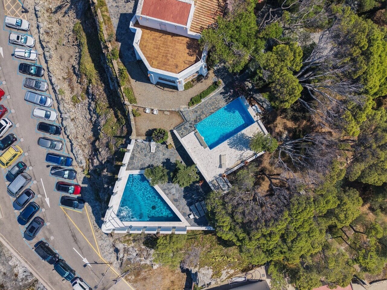 Ein Luftbild eines Anwesens mit zwei Schwimmbecken, einem Parkplatz und einem Gebäude mit einem Ziegeldach.