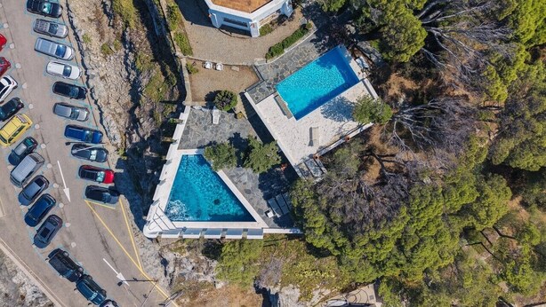 Vista aèria d'una propietat amb dues piscines, un aparcament i un edifici amb teulada d'estil clàssic.