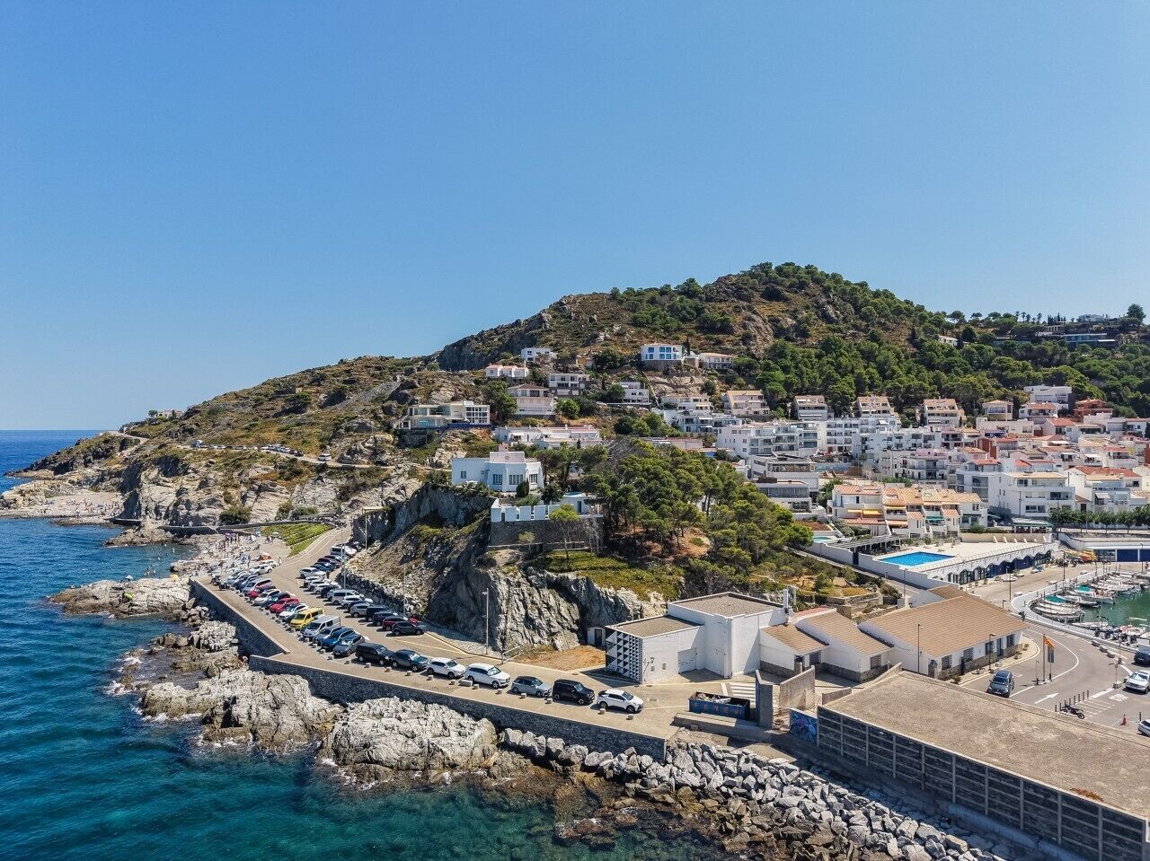 A coastal town with buildings on a hillside, a marina, and a parking area.
