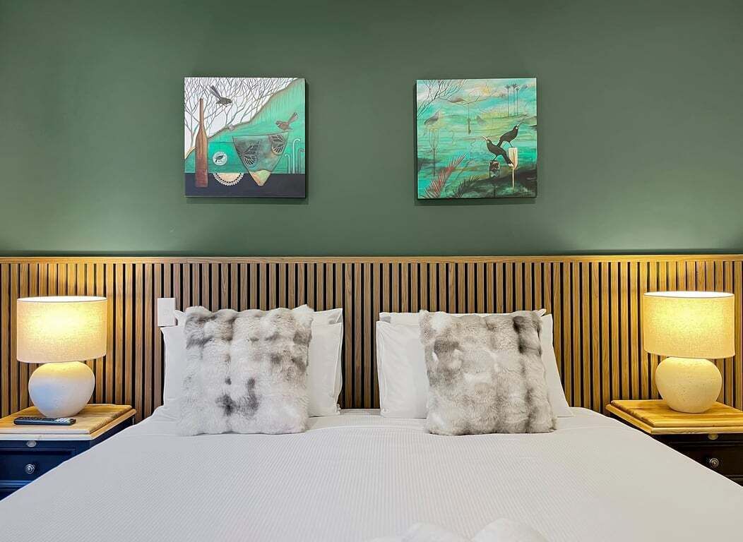 A hotel room with a bed, two nightstands, two lamps, and two wall-mounted paintings.