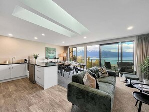 A modern interior with a kitchen, dining area, and seating by a large window overlooking a mountainous landscape. - Queenstown 3-Bed Getaway | Alpine Views (Queenstown)