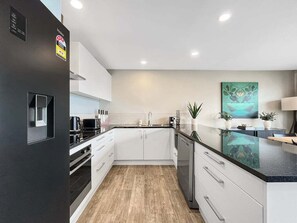 A modern kitchen with white cabinets, a black refrigerator, and a wooden floor. - Queenstown 3-Bed Getaway | Alpine Views (Queenstown)