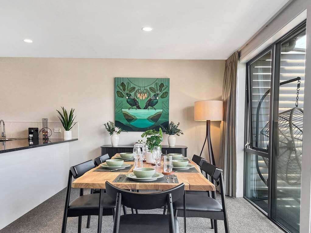A dining area with a table set for four, a painting on the wall, and a window with blinds.