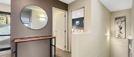 A hallway with a round mirror, a wooden bench, a door, and a small window with a picture.