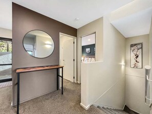 A hallway with a round mirror, a wooden bench, a door, and a small window with a picture. - Queenstown 3-Bed Getaway | Alpine Views (Queenstown)