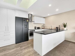 A modern kitchen with white cabinetry, a black refrigerator, a central island, and a stainless steel range hood. - Queenstown 3-Bed Getaway | Alpine Views (Queenstown)