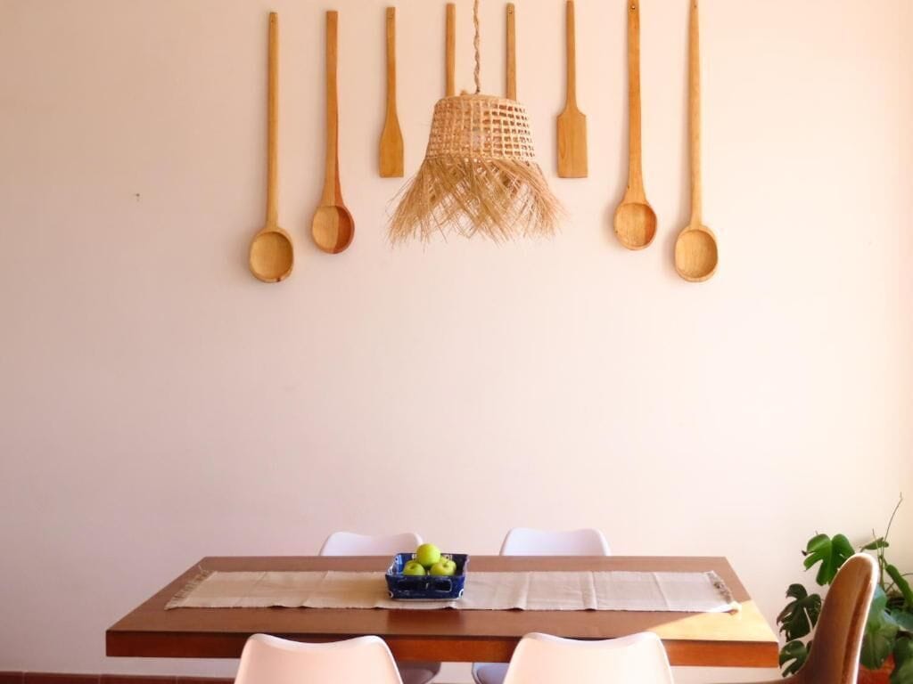 A dining area with a wooden table, white chairs, and a hanging wooden spoon collection.