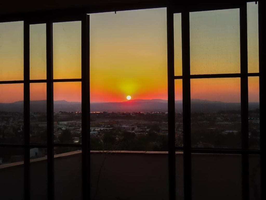 A sunset viewed through a window with a cityscape in the background.