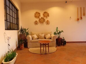 Uma sala de estar com um sofá, uma mesa redonda e várias plantas em vasos.