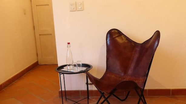 A chair with a unique design, a small round table with a bottle, and a tiled floor. - Casa Espiral (San Miguel de Allende)
