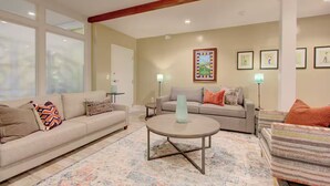 A living room with a sofa, armchair, and coffee table, with artwork on the walls and a window with blinds. - Walk to Charleston’s Best Dining and Entertainment (Charleston)