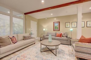 A living room with a sofa, armchair, and coffee table, with artwork on the walls and a window with blinds. - Walk to Charleston’s Best Dining and Entertainment (Charleston)