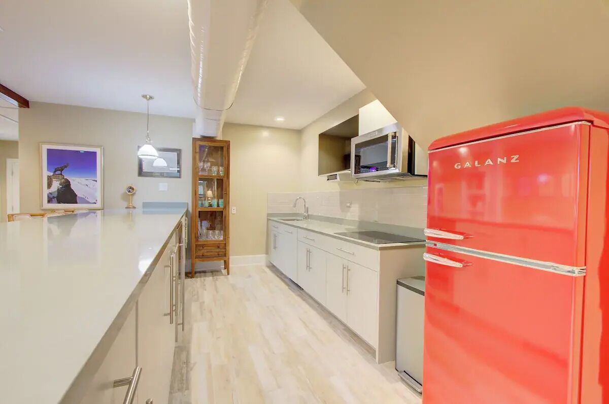 Une cuisine moderne avec un réfrigérateur rouge, des meubles blancs et un coin bar en bois.