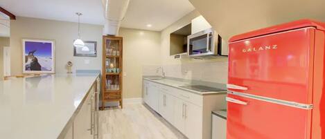 Une cuisine moderne avec un réfrigérateur rouge, des meubles blancs et un coin bar en bois.
