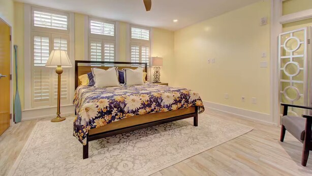 A bedroom with a bed, two bedside lamps, a ceiling fan, and a window with blinds. - Walk to Charleston’s Best Dining and Entertainment (Charleston)