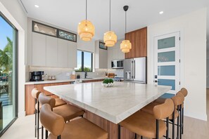 Une cuisine moderne dotée d’un grand îlot central, de meubles en bois, d’appareils électroménagers en acier inoxydable et de luminaires suspendus.