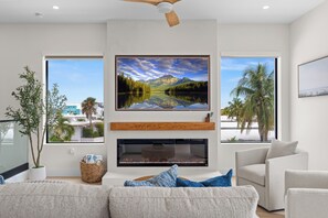 A modern living room with a fireplace, a mounted TV, and a large window offering a view of a lake and mountains.