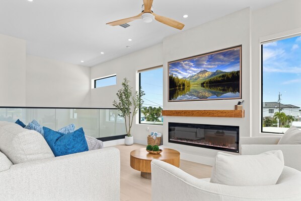 A modern living room with a fireplace, a large window with a mountain view, and a ceiling fan.