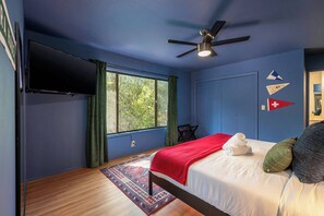 Ein Schlafzimmer mit einem Bett, einem Deckenventilator, einem Fernseher und einem Fenster mit Vorhängen.