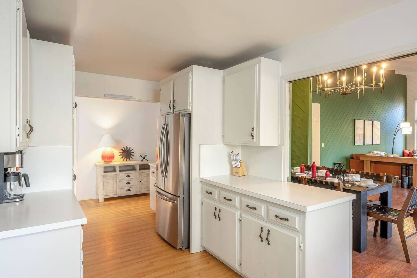 A modern kitchen with white cabinetry, a stainless steel refrigerator, and a dining area with a wooden table and chairs.